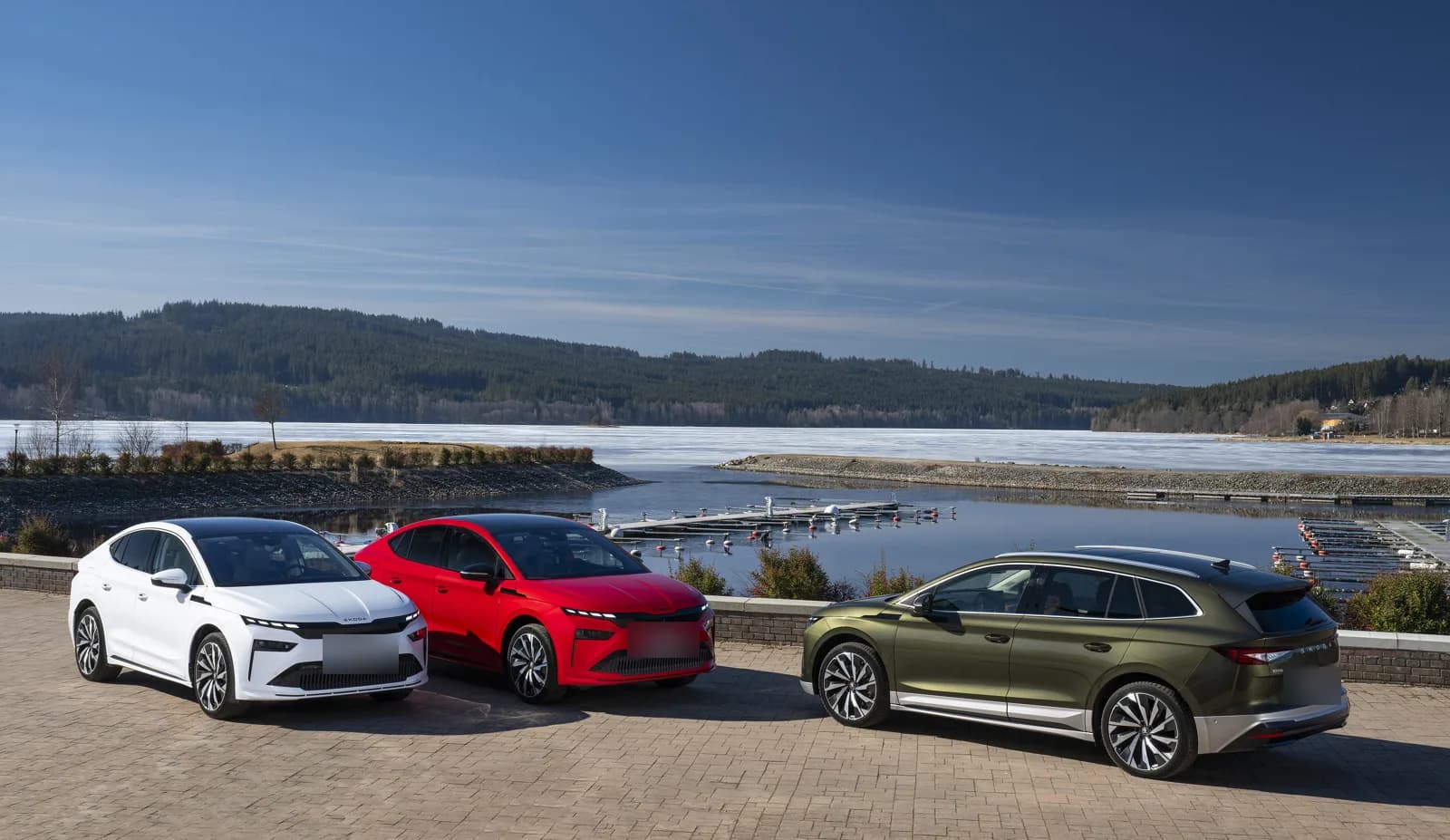 Skoda Enyaq and Enyaq Coupé parked by a lake, front three-quarter view